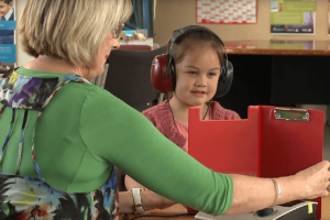 A vision hearing technician testing a young girl with headphones on